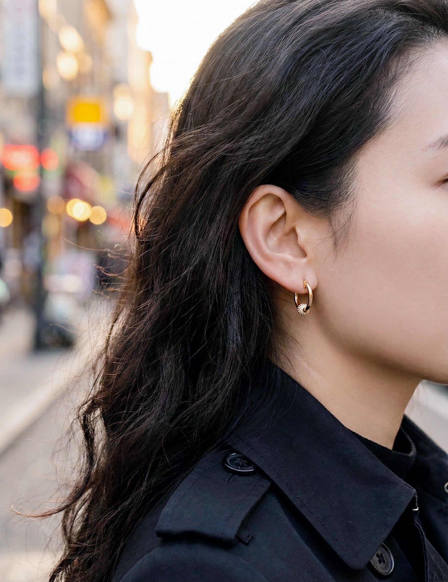Woman wearing gold pave huggie earrings street style black coat