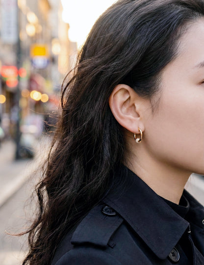 Woman wearing gold pave huggie earrings street style black coat