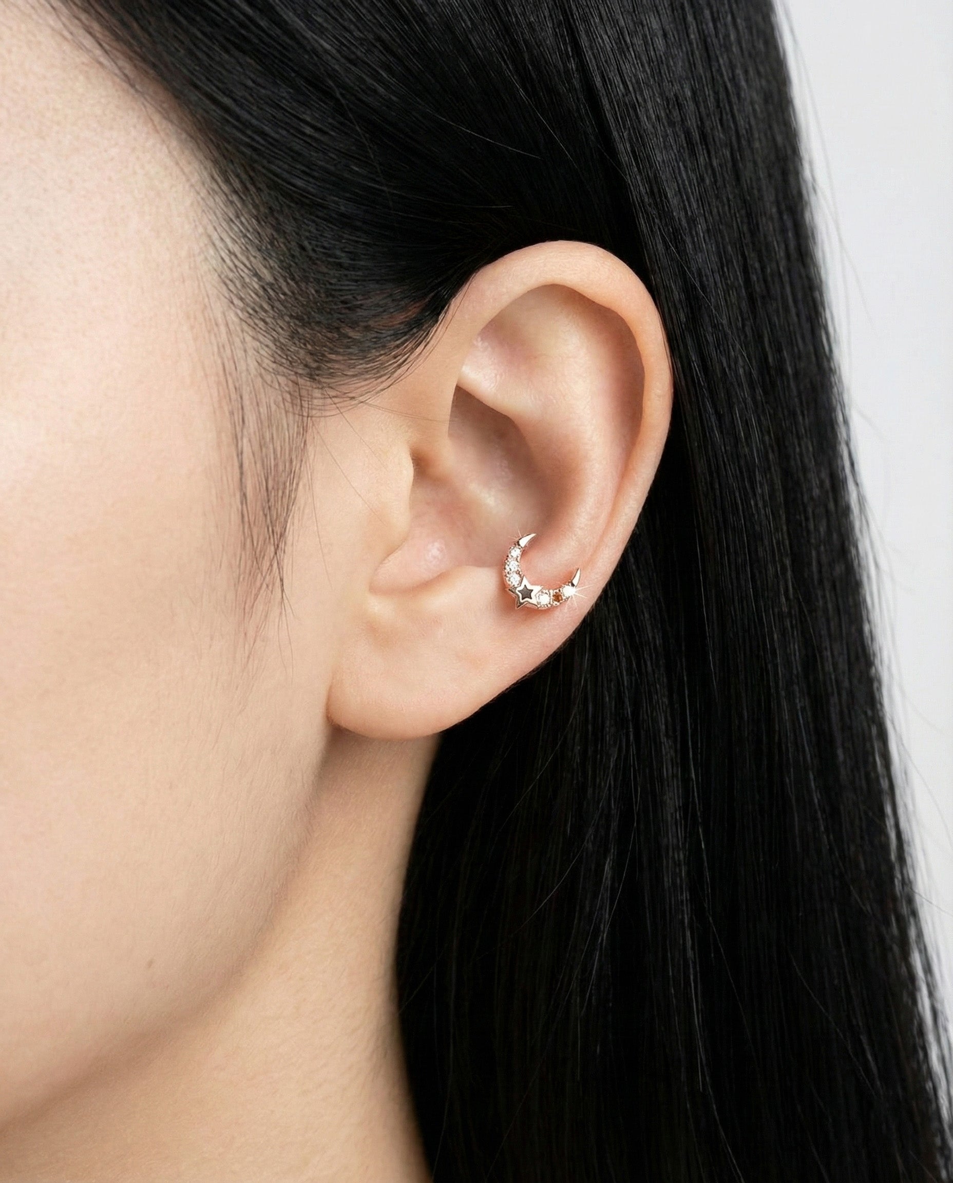 Zoomed-out view of rose gold moon cartilage piercing with a sparkling finish on a minimalist ear styling.