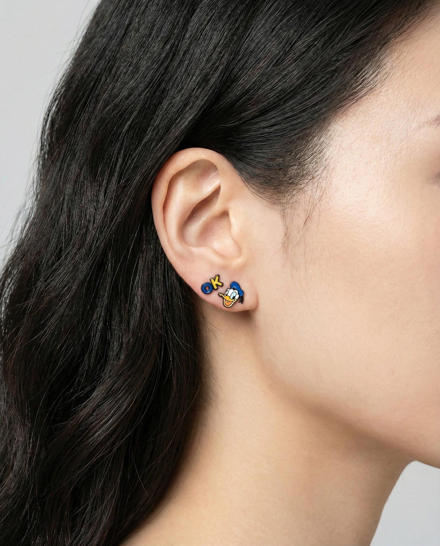 Close-up of woman wearing Donald Duck and OK sign mismatched earrings - Y2K kawaii style