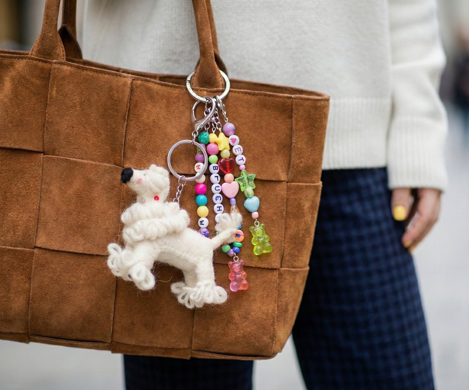 Cute felt poodle keychain with colorful letter beads and gummy bear charms attached to a brown suede tote bag