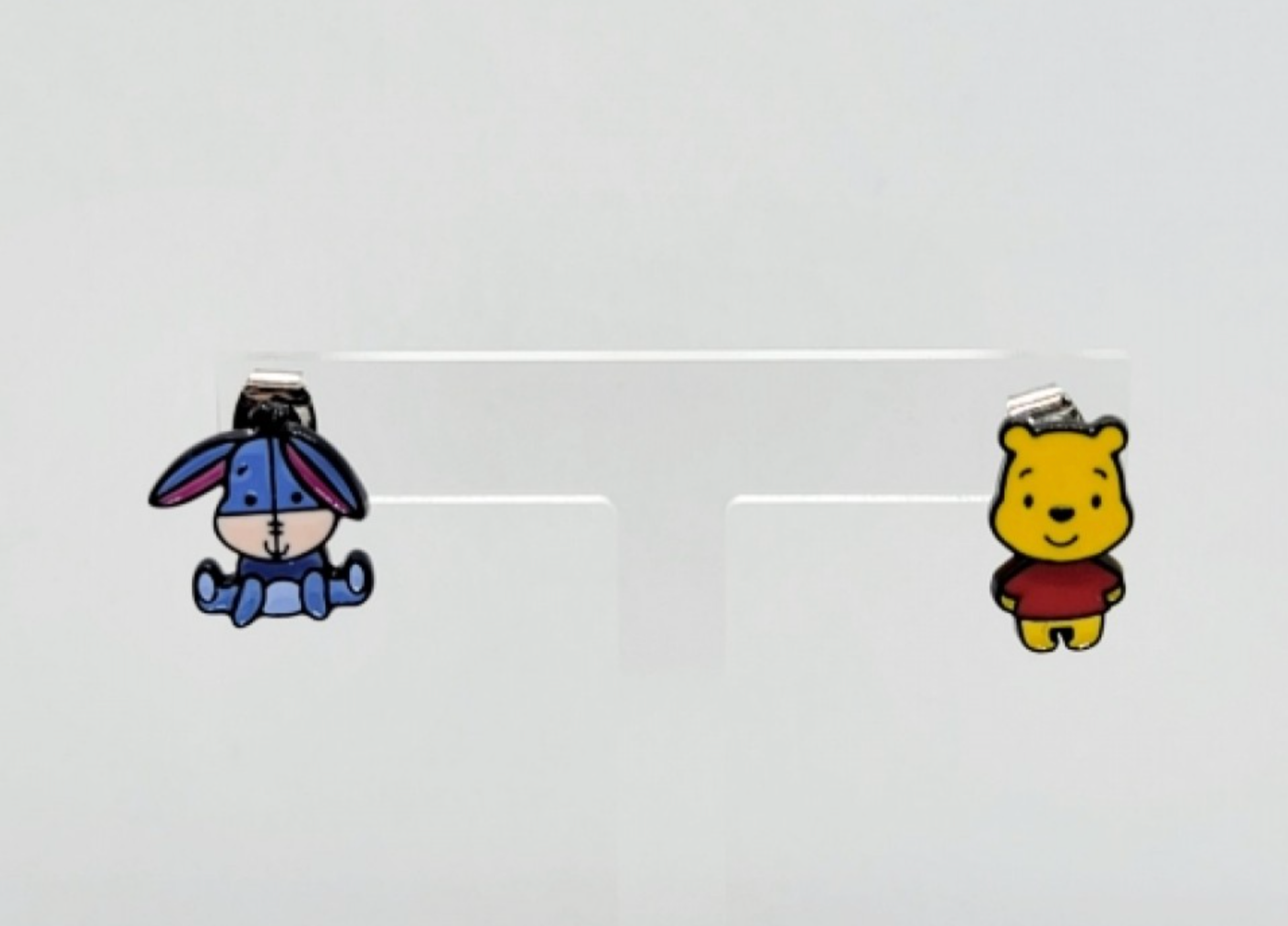 Front view of mismatched Pooh and Eeyore character earrings on an acrylic display stand