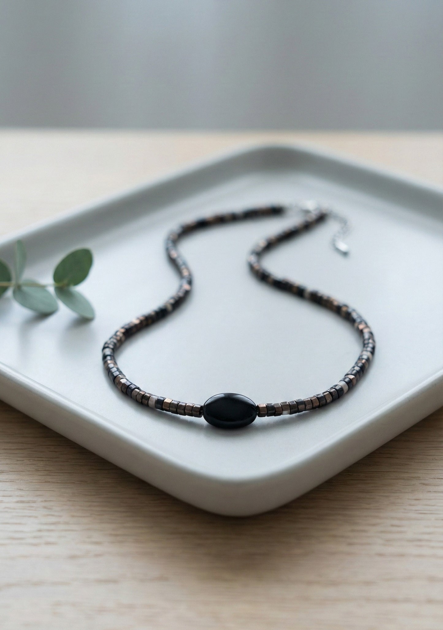 Black onyx gemstone choker with gray shell heishi beads on white plate"