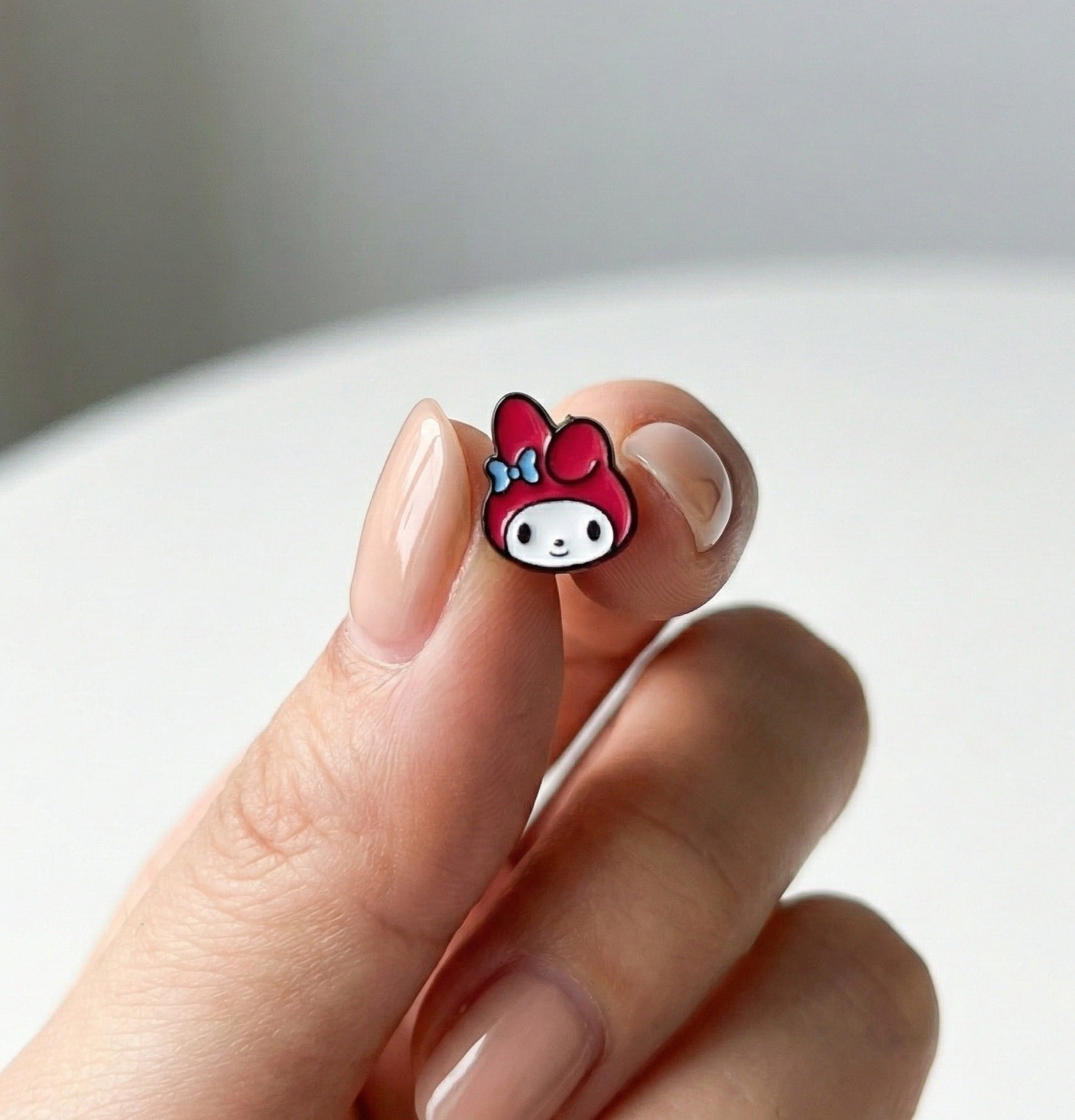  Hand holding single My Melody enamel stud earring showing pink hood and blue ribbon detail
