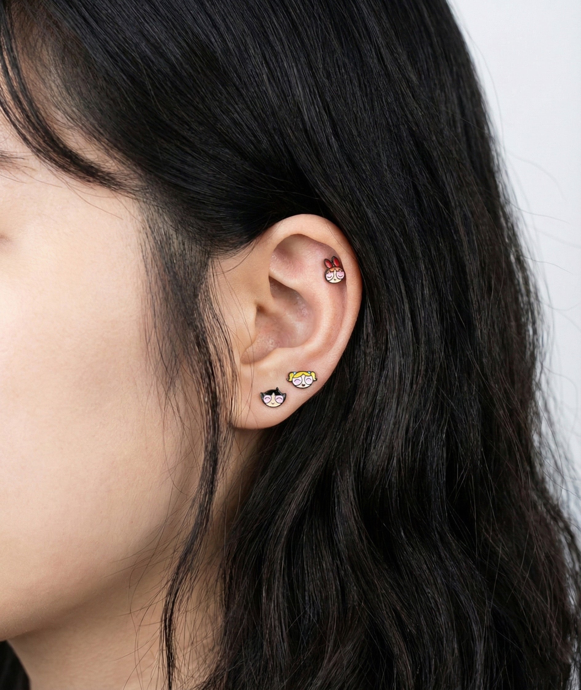 Full ear styling with three Powerpuff Girls barbell studs - layered on lobe outer conch and helix piercings