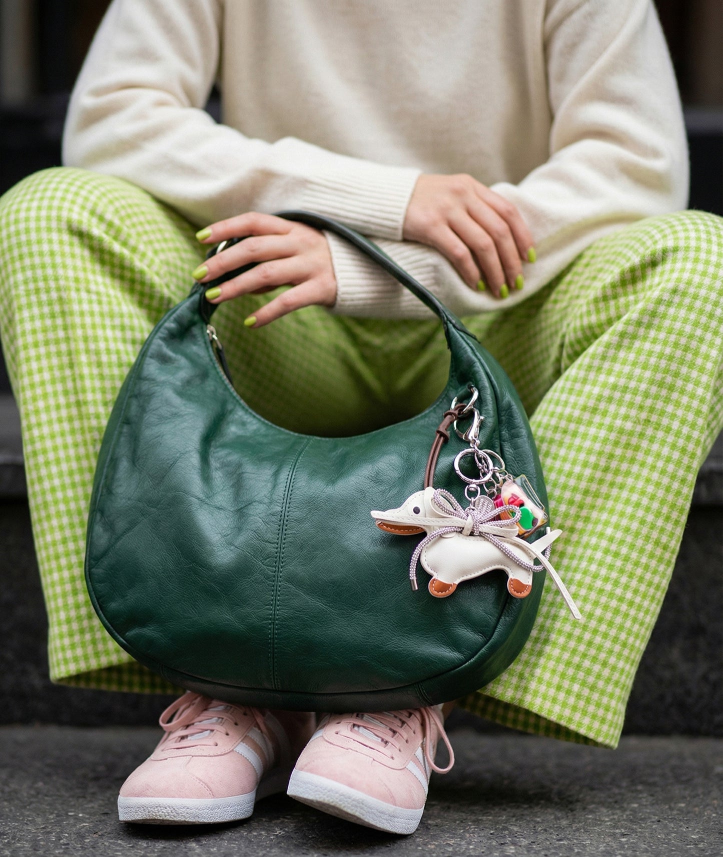 White leather Dachshund keychain with crystal ribbon on green bag held by person in cream knit sweater and gingham pants