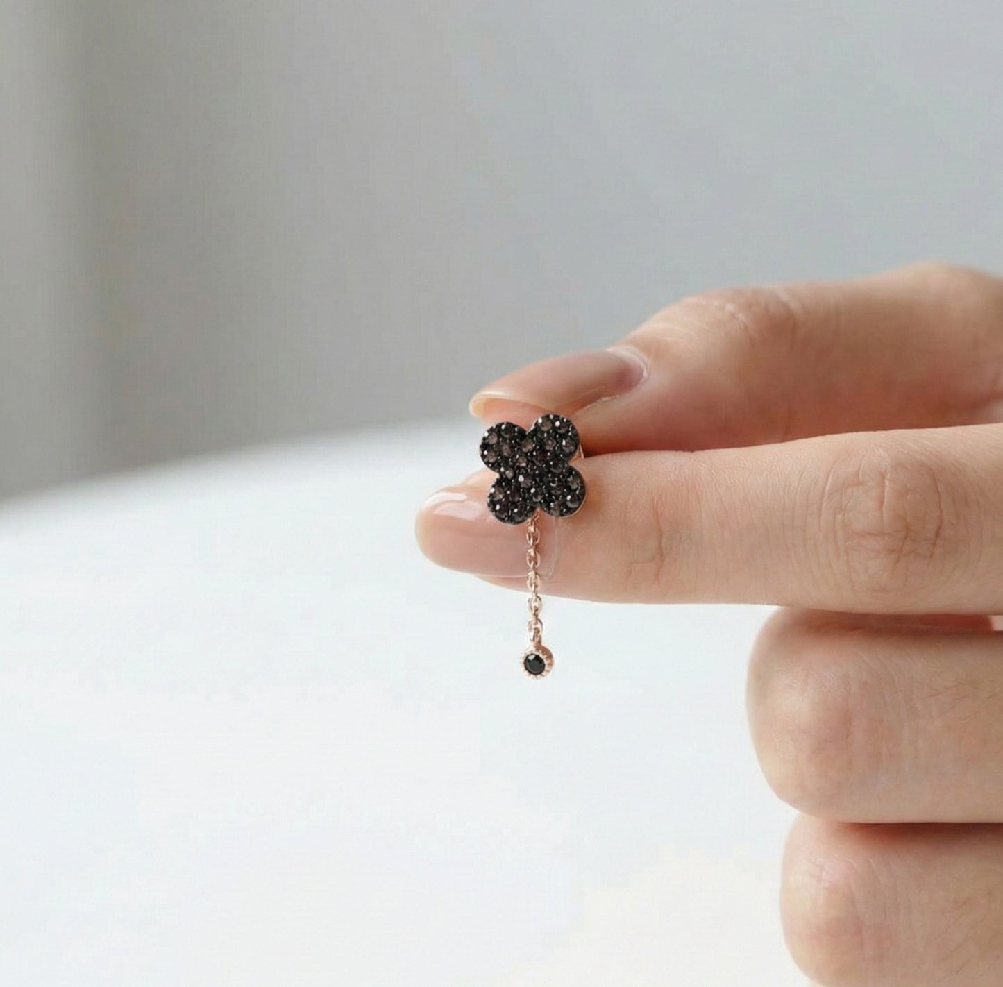Flower-shaped earring with black stones held by a hand against a neutral background