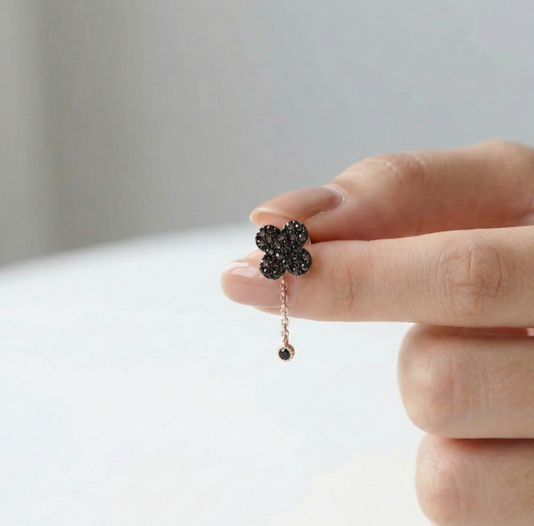 Flower-shaped earring with black stones held by a hand against a neutral background