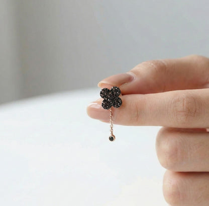 Flower-shaped earring with black stones held by a hand against a neutral background