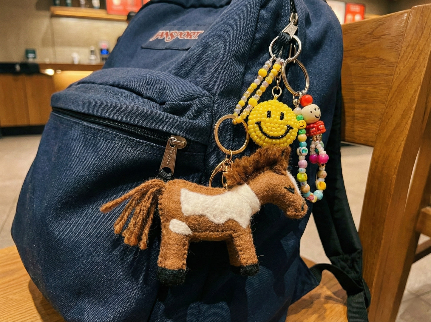 Brown felt horse keychain with smiley beaded charm attached to navy blue backpack