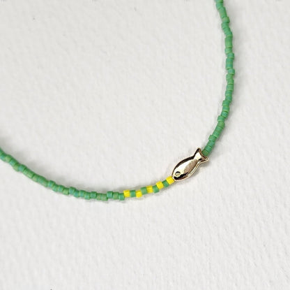 Fresh green seed bead necklace with gold fish charm and yellow accent beads close-up view