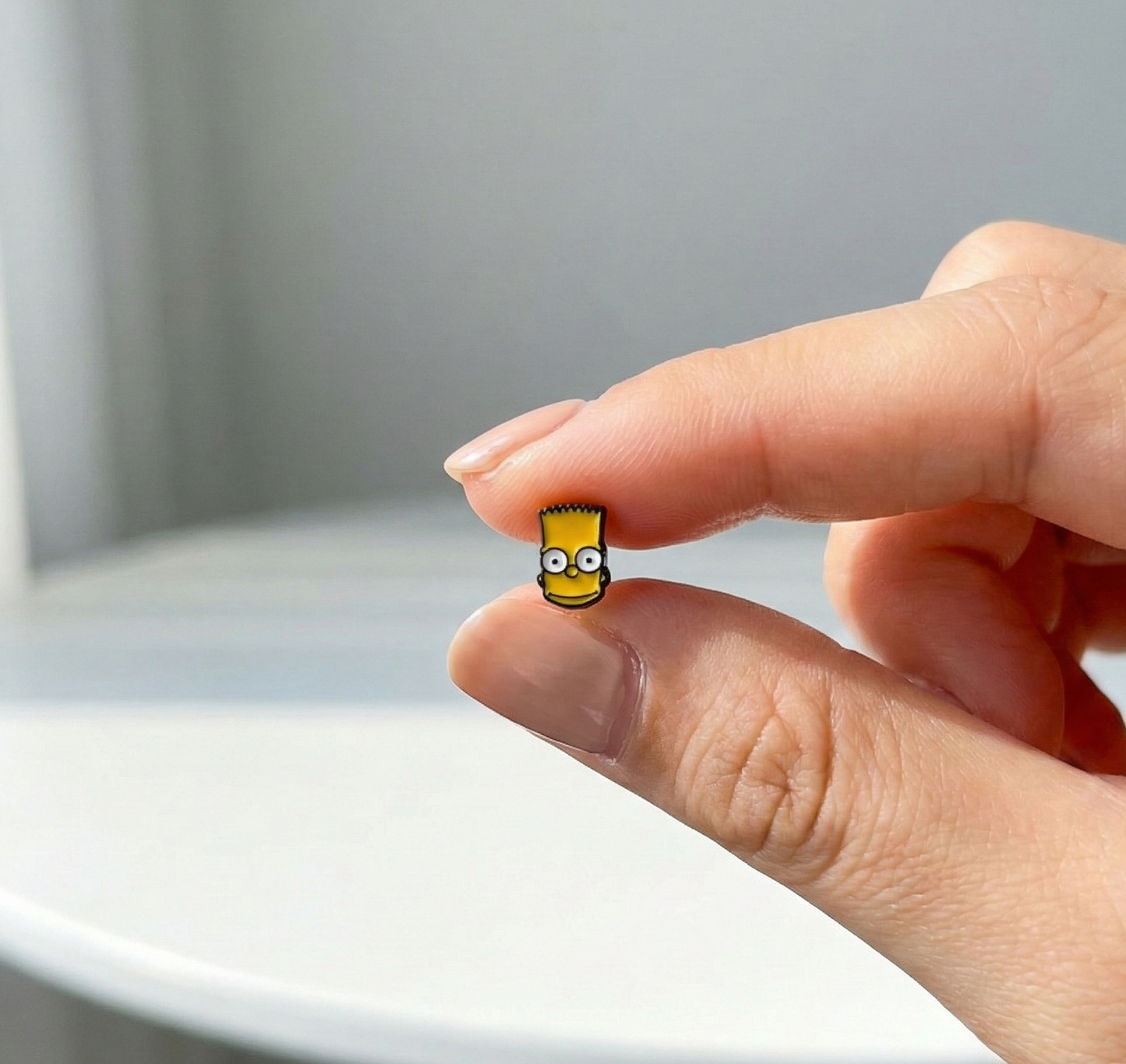Close-up of tiny Bart Simpson enamel stud earring held between fingers, showing detailed facial expression
