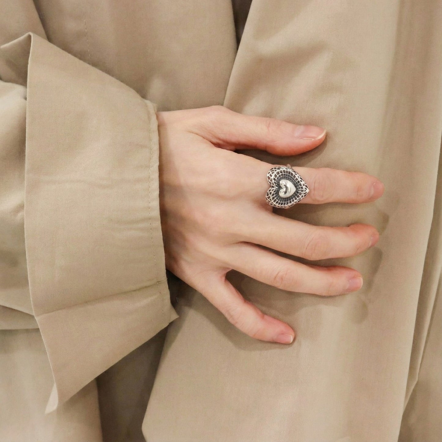 Side angle of handmade silver filigree heart ring on middle finger with beige blouse showing coquette aesthetic