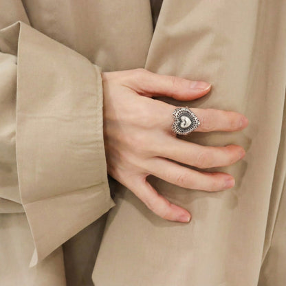 Side angle of handmade silver filigree heart ring on middle finger with beige blouse showing coquette aesthetic