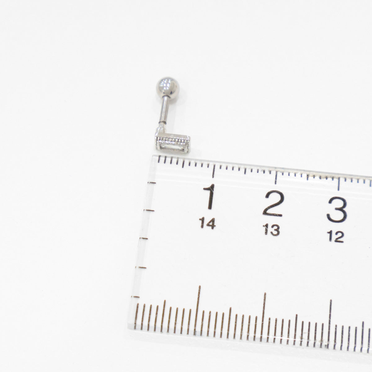 Side view of a silver rectangular CZ barbell earring next to a ruler for size reference.