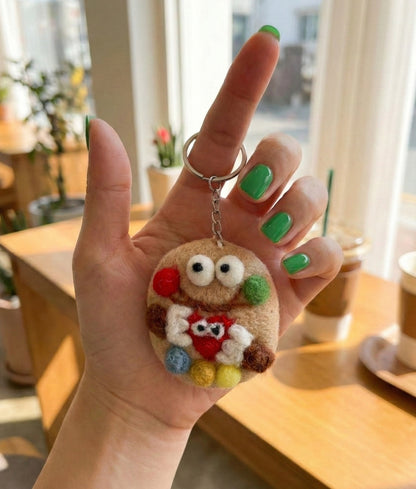 Hand holding cookie monster wool felt keychain with green nail polish, showing size and texture