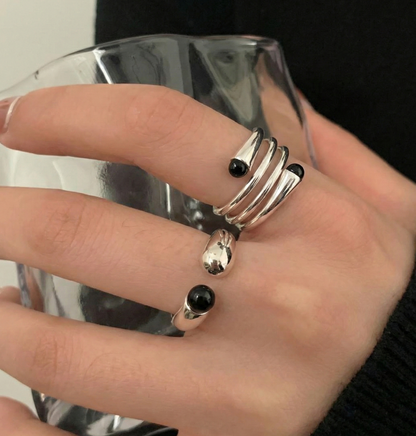 Hand model holding glass wearing 925 sterling silver black onyx spiral and single open rings layered — index and middle finger styling