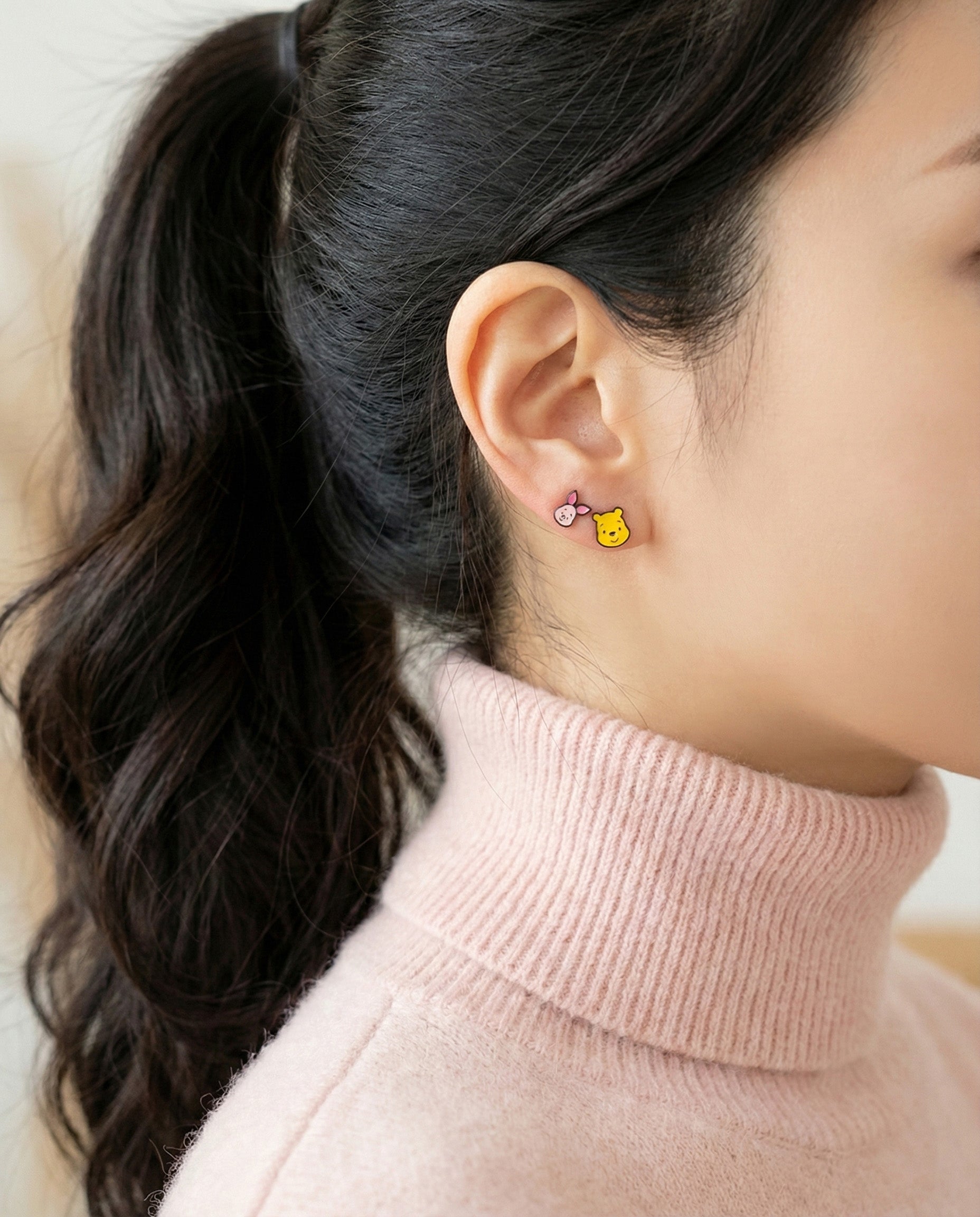 Close-up of Pooh and Piglet enamel stud earrings on model's ear