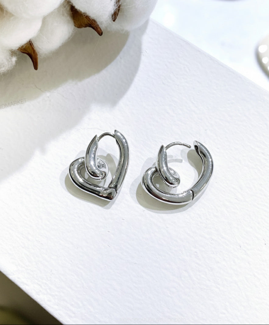 Pair of silver twisted heart huggie hoop earrings flat lay on white background, Korean jewelry