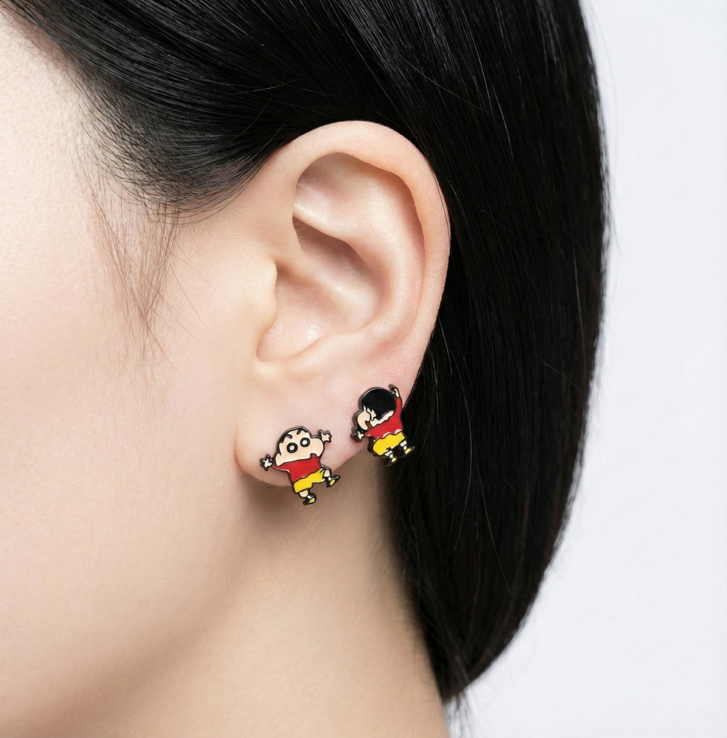 Crayon Shin-chan inspired child figure stud earrings in red and yellow worn on the earlobe.