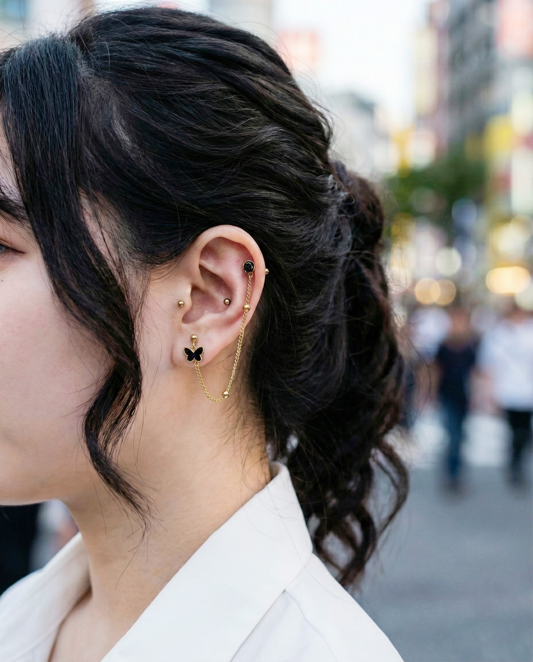 Gold chain piercing with black butterfly and rose stud worn on ear with casual hairstyle