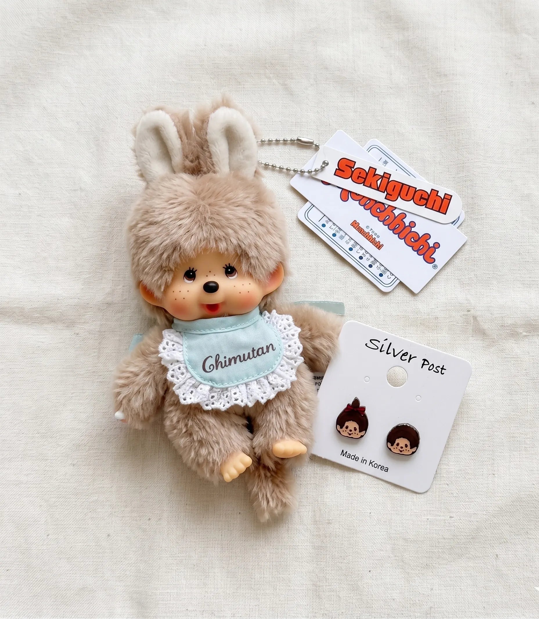 Flat lay detail shot Chimutan pink plush keychain with Monchhichi face earrings and flower bead necklace, K-style accessories — 8ttitto8