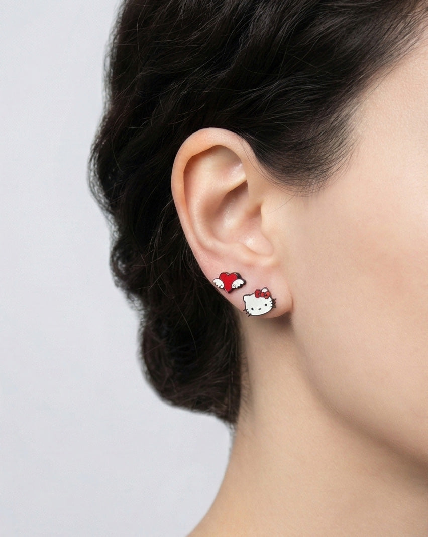 Side profile of woman wearing Hello Kitty face and winged heart enamel earrings, adorable mismatched pair design, 925 silver posts, Korean kawaii jewelry for everyday