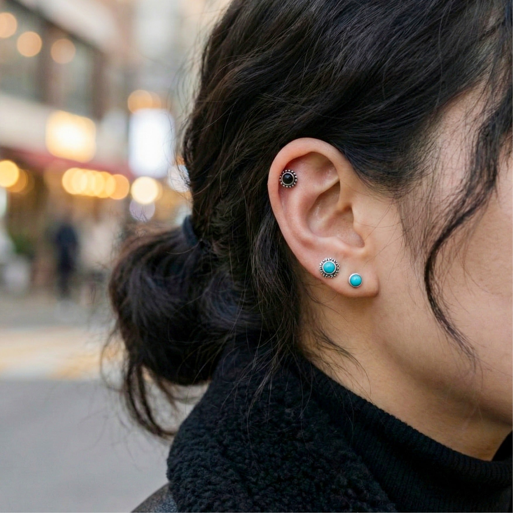  Woman wearing turquoise barbell studs in lobe and helix piercings, outdoor street style
