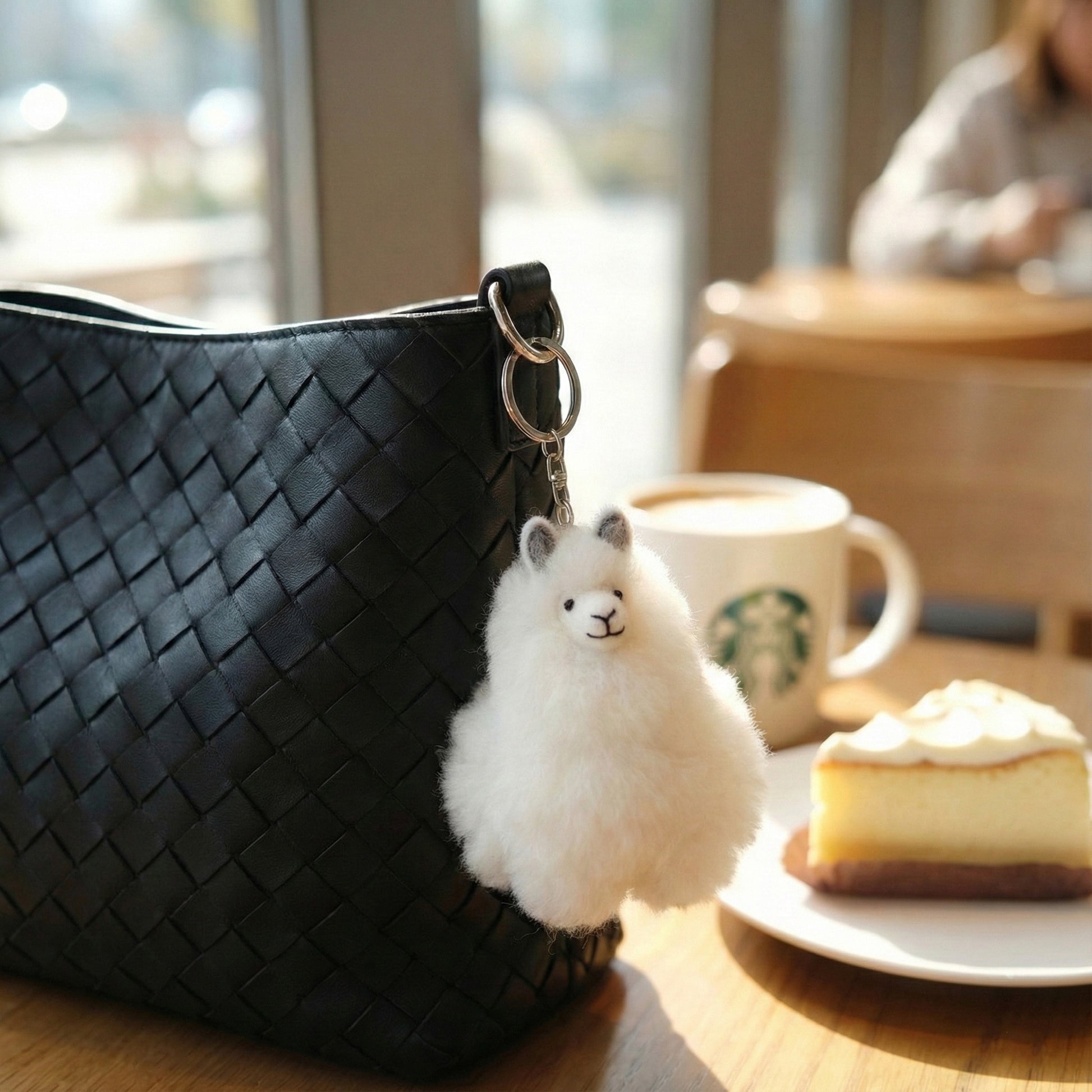 White alpaca fur keychain hanging from black woven bag at café