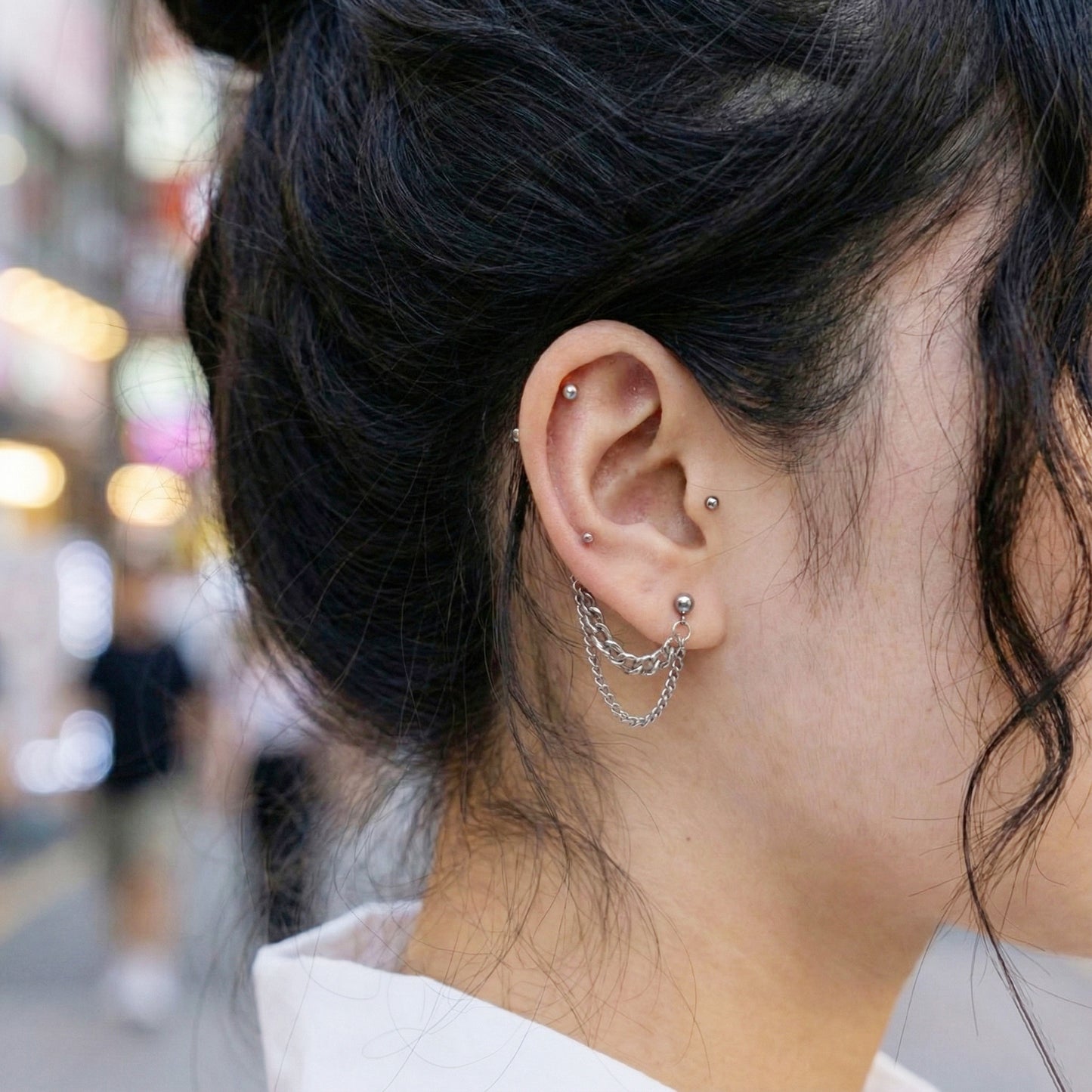 Silver surgical steel double chain piercing on ear with urban street background
