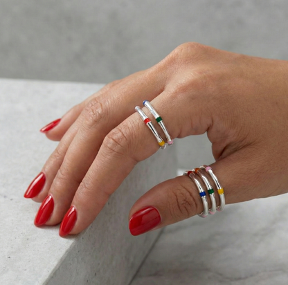 Model with red nail polish wearing layered multicolor enamel 925 silver stacking rings on two fingers, marble background