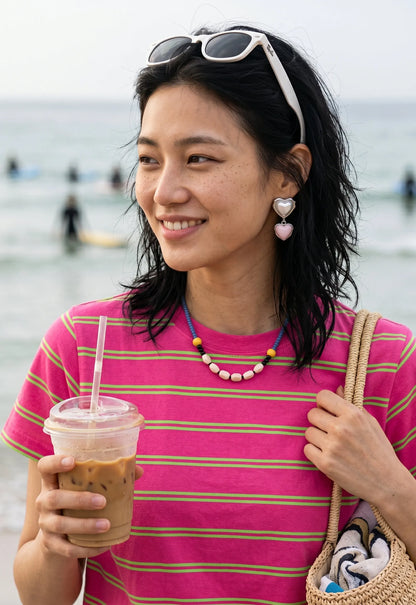 Pink heart drop earrings styled with colorful beaded necklace, K-style jewelry for beach day look.