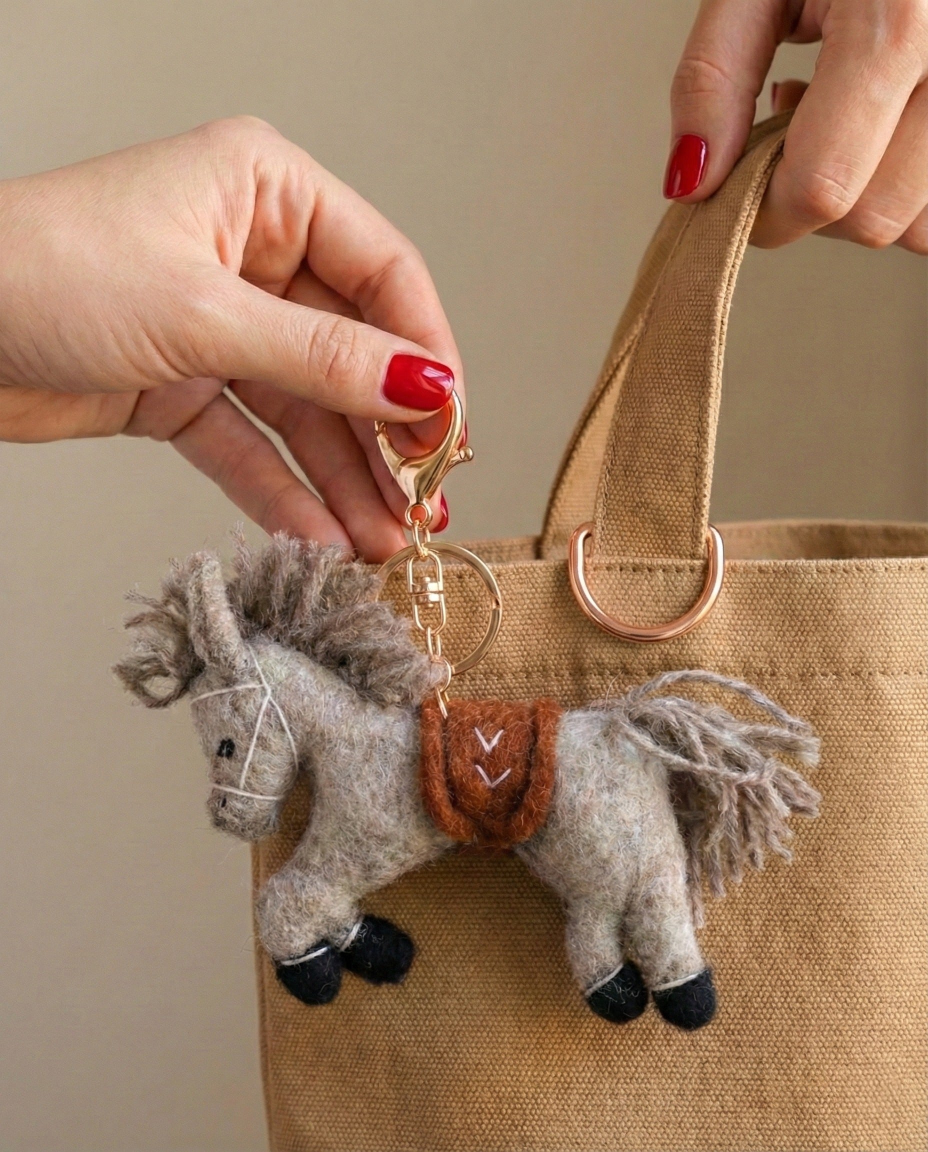 Close-up of grey felt horse keychain held in hand showing detailed mane texture and embroidered saddle
