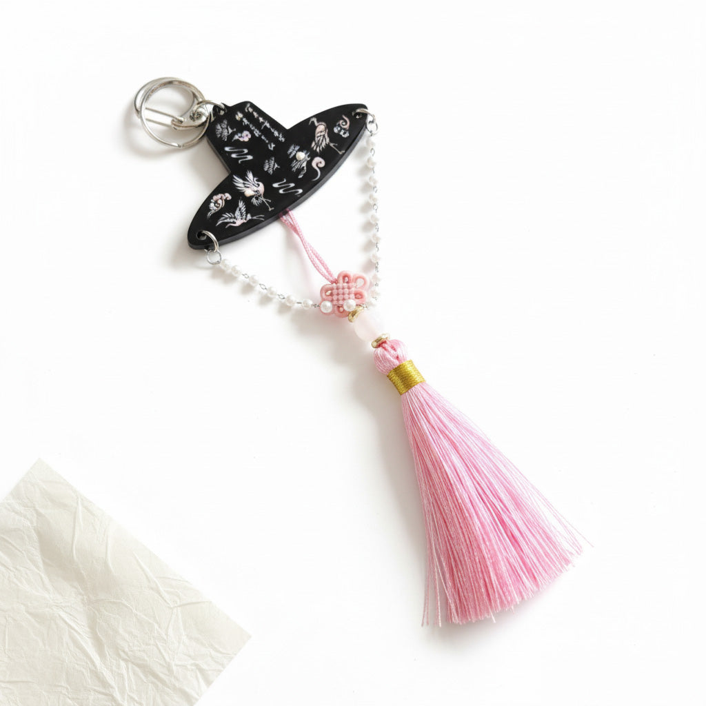 The pink gat keychain with flamingo inlays, floral knot, pearls and silk tassel, dangling in soft daylight.