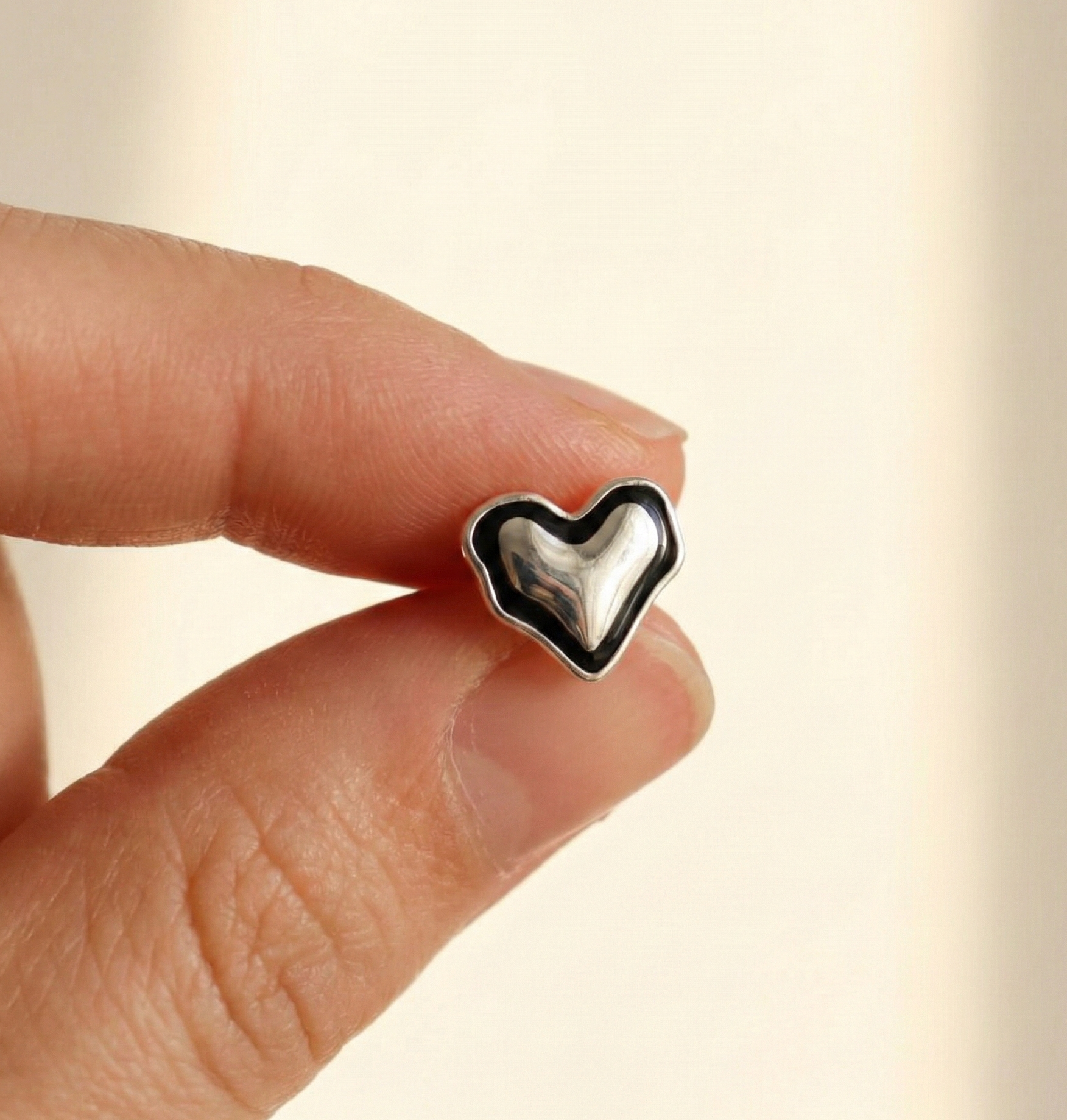 Hand holding single 925 sterling silver black enamel chunky heart earring to show actual size approximately 12mm