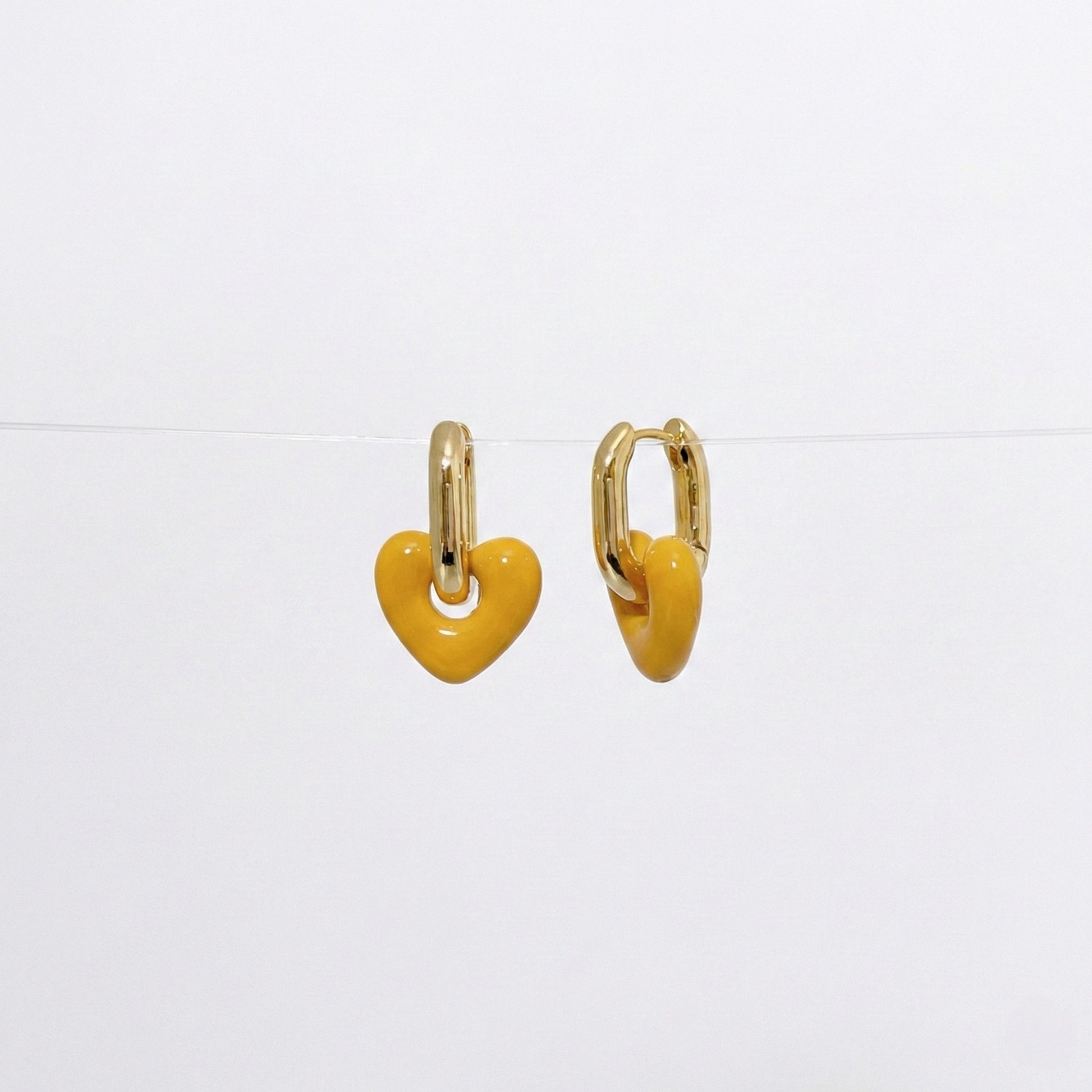 Mustard yellow puffy heart drop earrings with gold-tone brass huggie hoops on white background