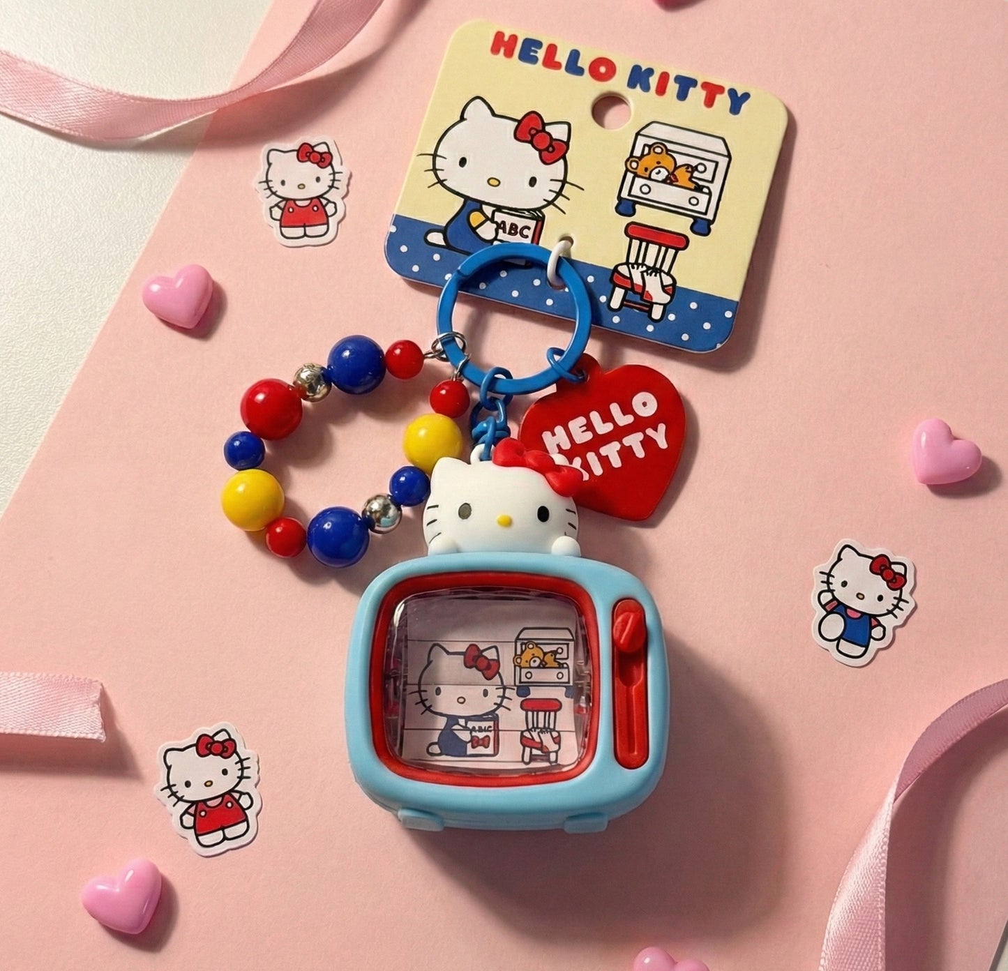 Sanrio Hello Kitty retro TV figure keychain on pink background with Hello Kitty stickers and ribbon — Y2K kidcore kawaii bag charm flat lay