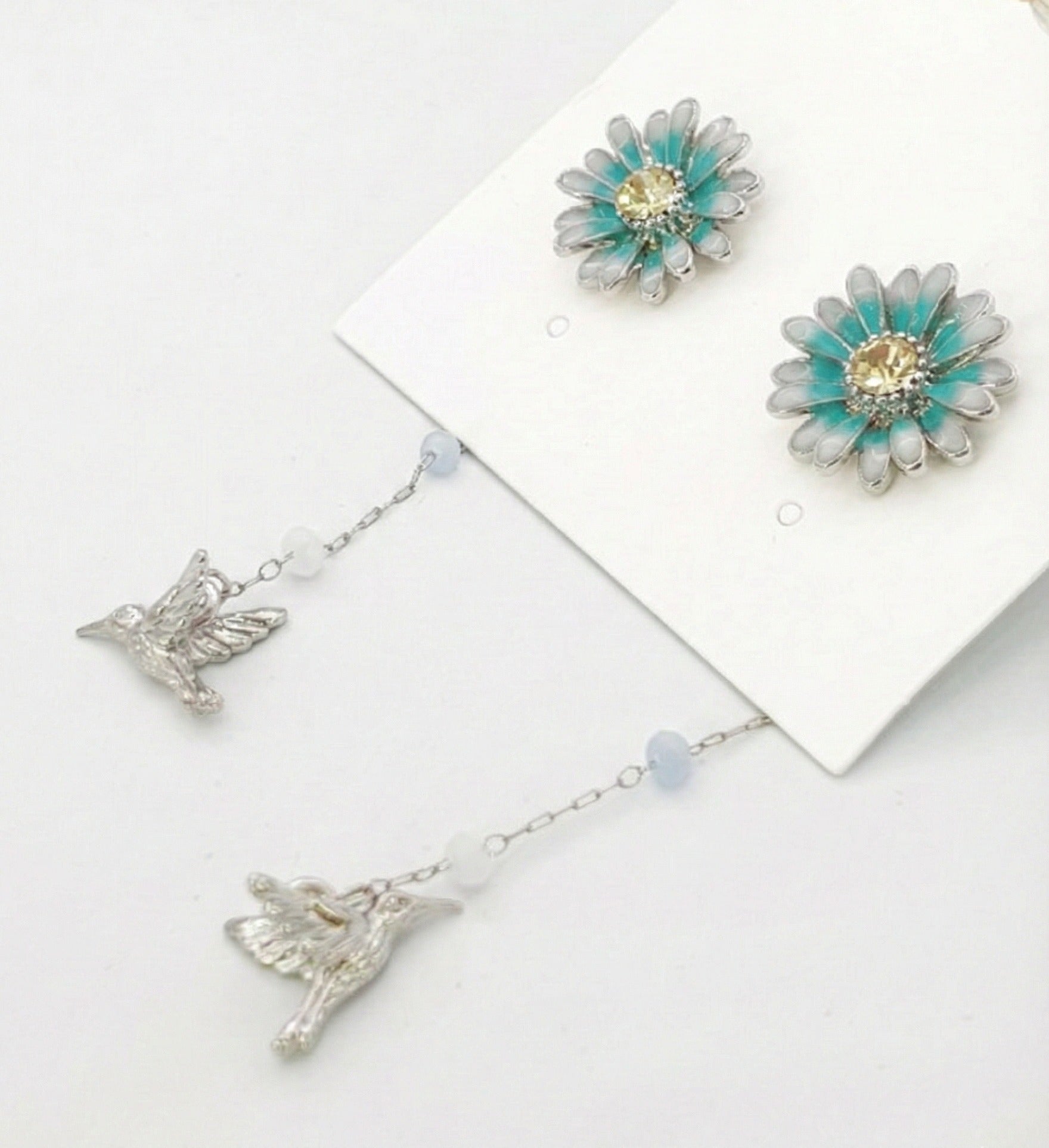 Close-up of silver daisy stud with mint blue petals and hummingbird charm