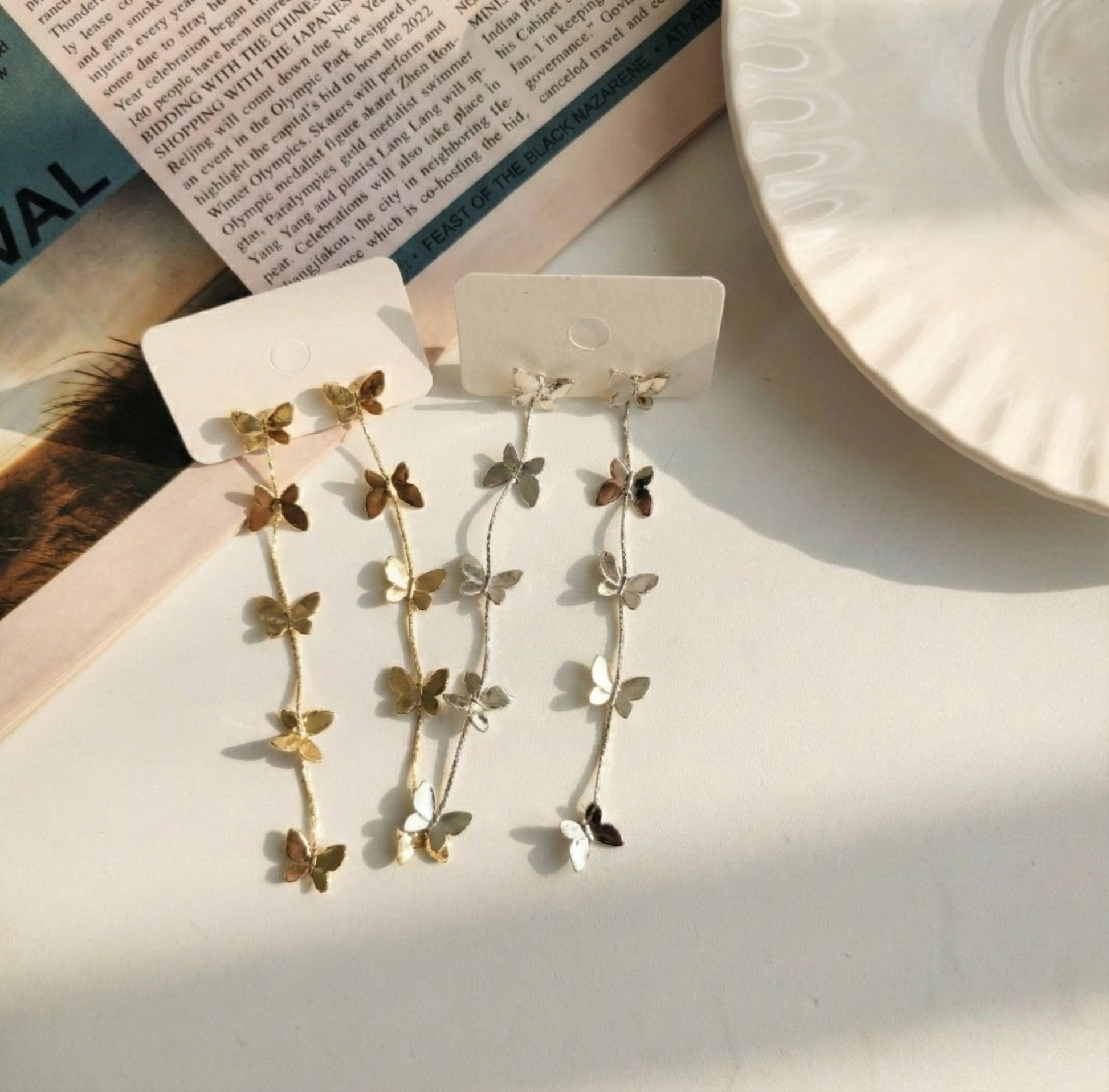 Flat lay of gold and silver butterfly drop earrings on white display cards
