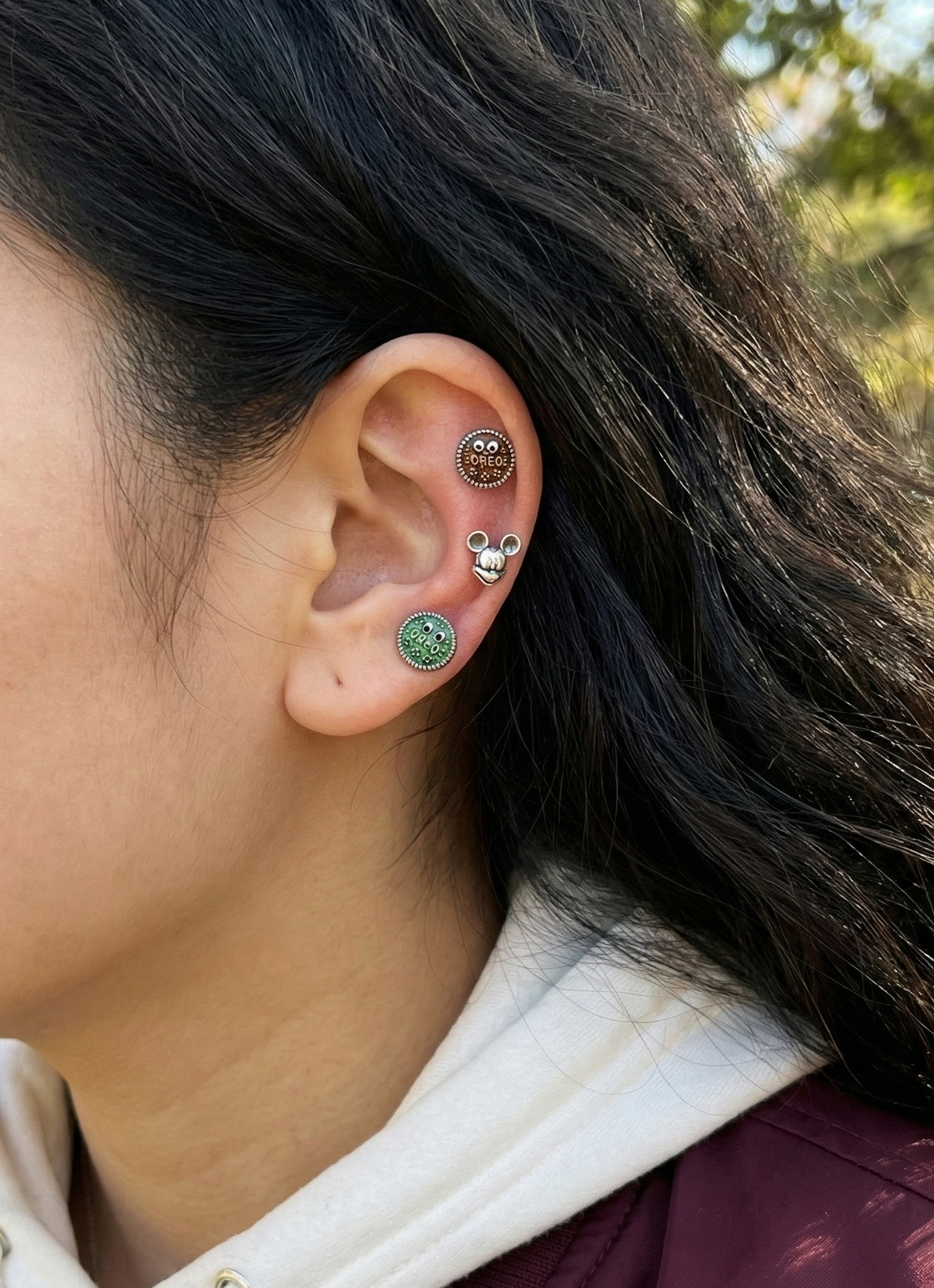 Ear styling with three piercings - brown Oreo on upper cartilage, Mickey on conch, green Oreo on lobe
