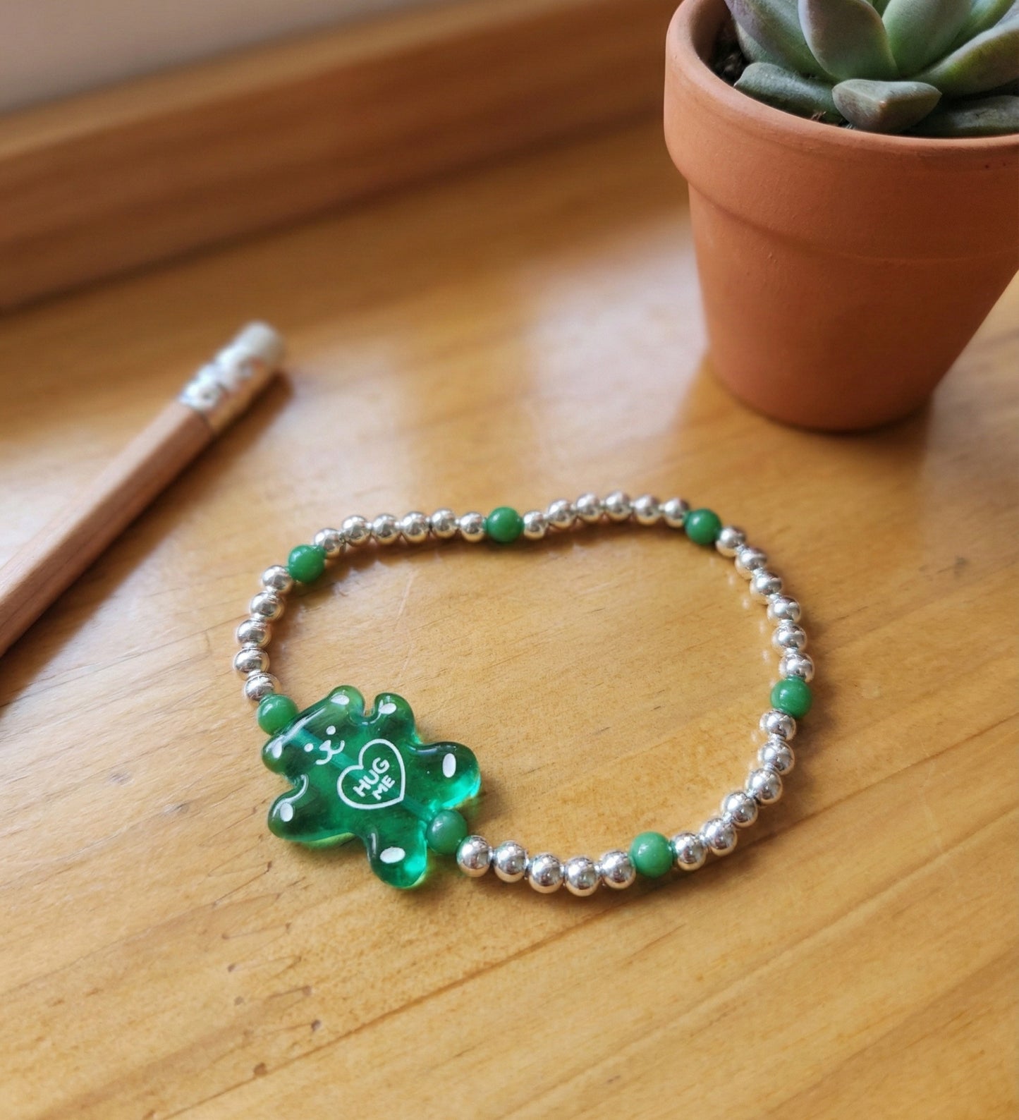 Transparent green gummy bear 925 silver ball bracelet on wooden desk with succulent plant