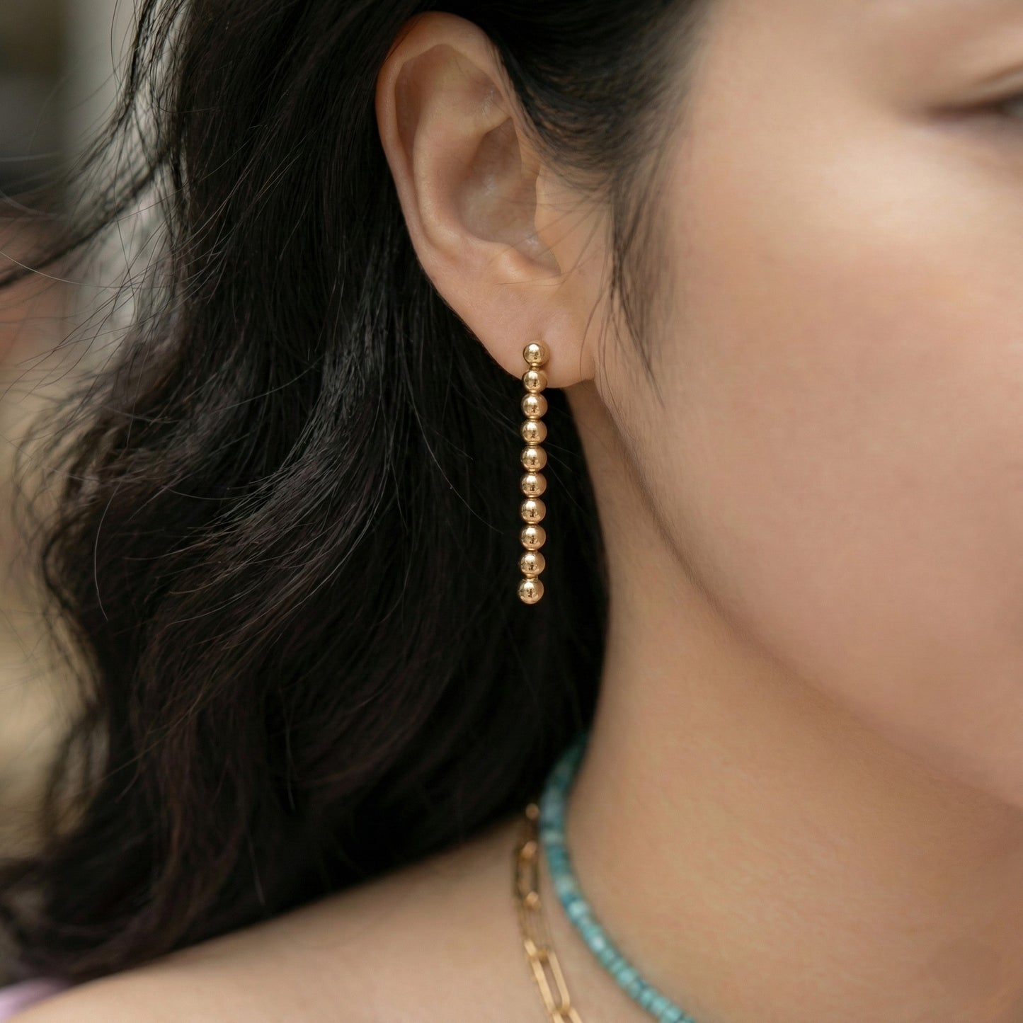 Side view of woman wearing gold ball drop earrings with turquoise necklace