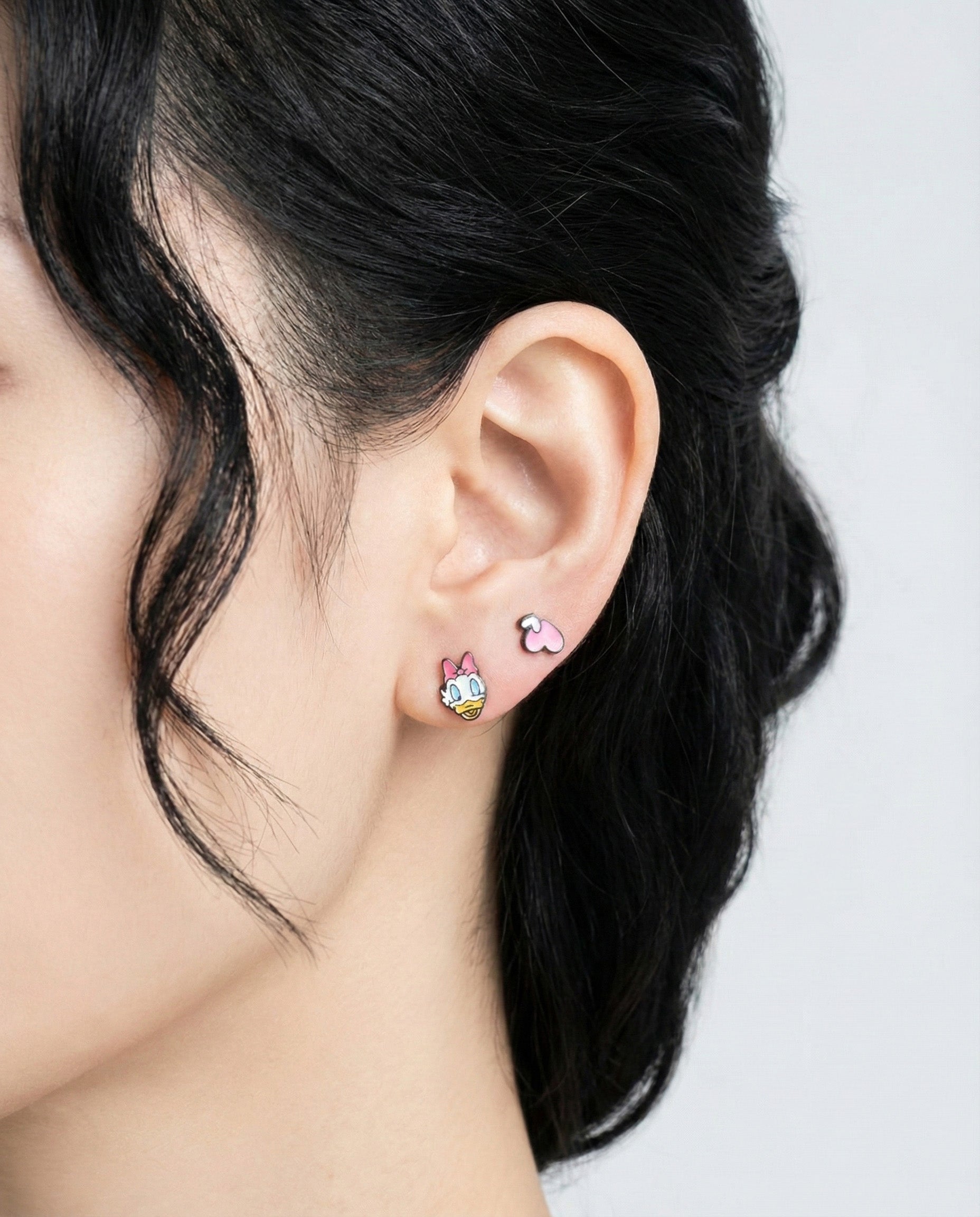 Woman modeling Daisy Duck and heart enamel earrings - romantic pink character studs on ear