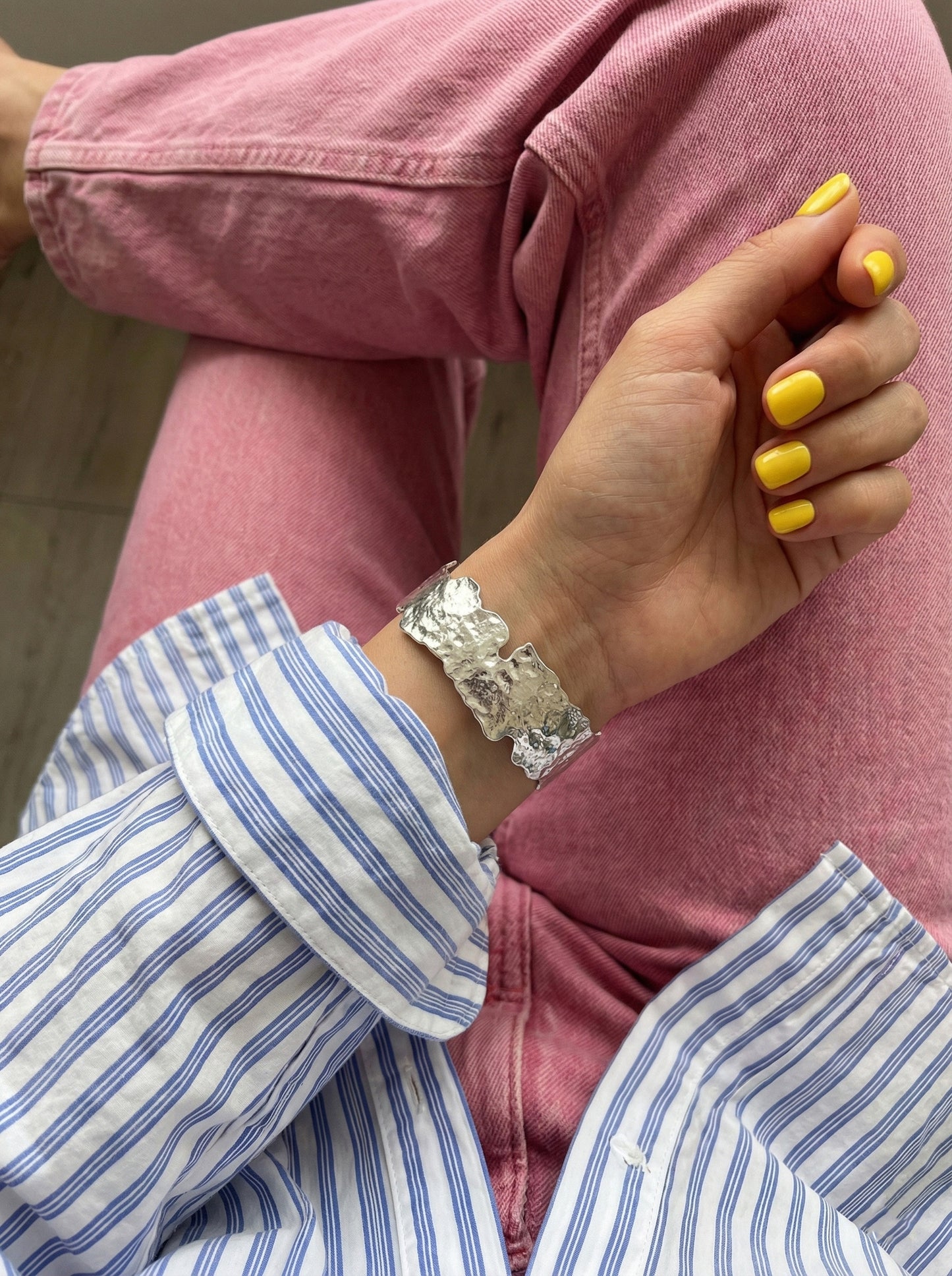 Wide silver cuff bracelet on bare wrist with yellow nails - textured metal bangle