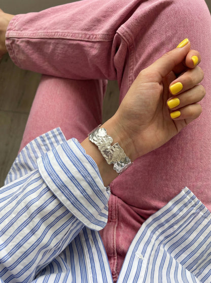 Wide silver cuff bracelet on bare wrist with yellow nails - textured metal bangle