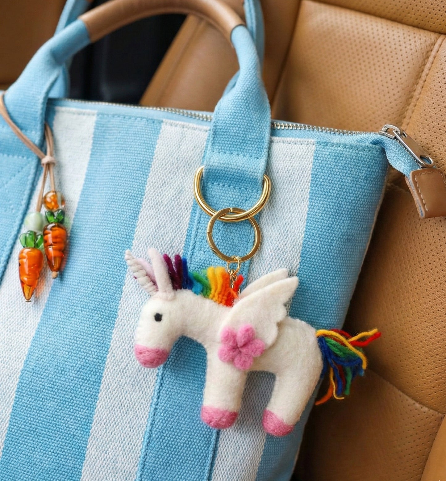 Rainbow unicorn felt keychain attached to blue striped canvas tote bag with carrot charm accessories