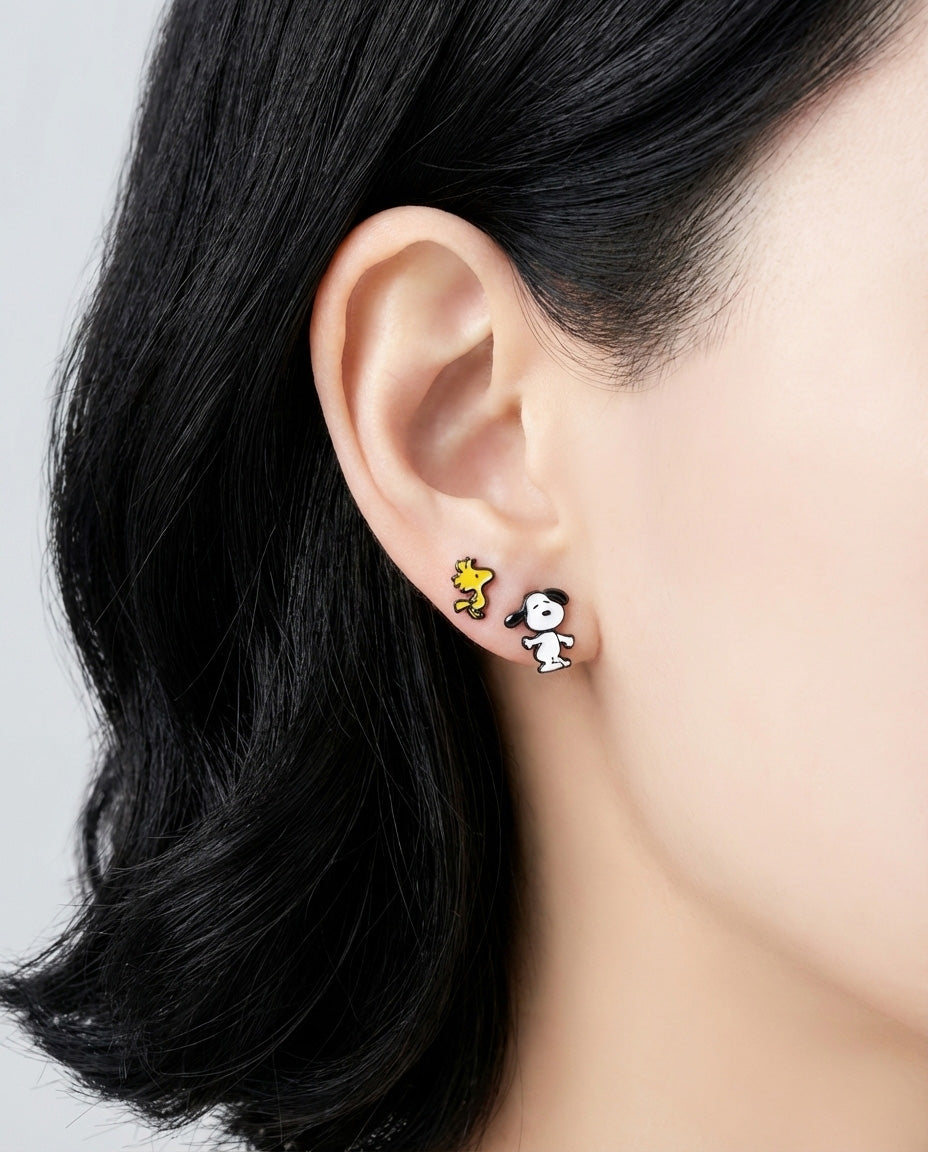 Model wearing Snoopy and Woodstock asymmetric earrings on ear