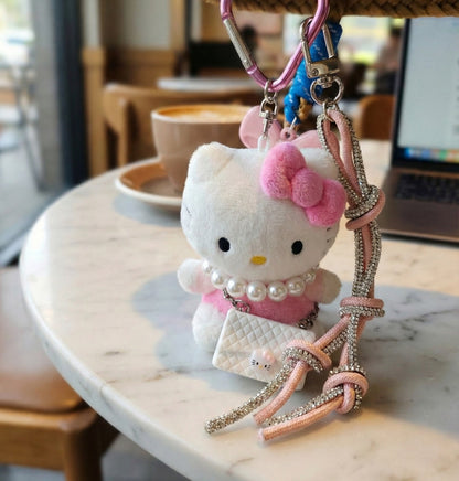 Close-up of Hello Kitty bag charm held in hand showing pearl necklace and quilted mini bag detail with heart carabiner clip