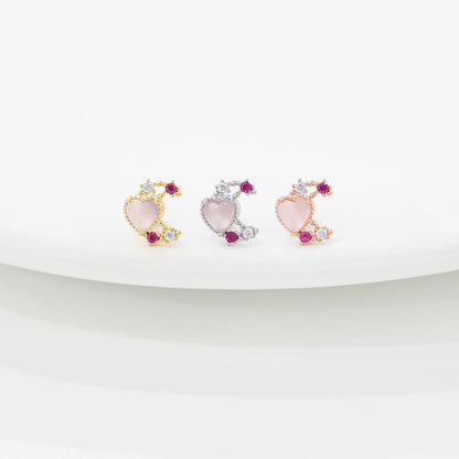 Three pink rose quartz moon heart barbell studs in gold, silver, and rose gold plating on white curved surface