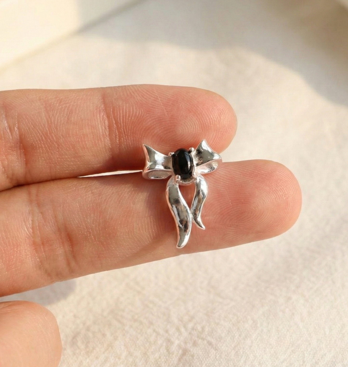 Single 925 silver black agate bow earring held between fingers to show size — approximately 2cm handmade jewelry